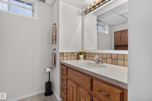 Bathroom vanity with a light-toned countertop, integrated sink, and wood-finish cabinetry - 17603 85 Avenue Nw, Edmonton, AB 