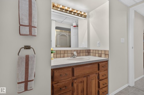 Bathroom vanity featuring a wood-finish cabinet with multiple drawers, a solid surface countertop, and an integrated sink - 17603 85 Avenue Nw, Edmonton, AB 
