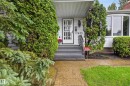White siding exterior with a covered entryway, showcasing a bay window, a front door with decorative glass, and established evergreen landscaping - 17603 85 Avenue Nw, Edmonton, AB 