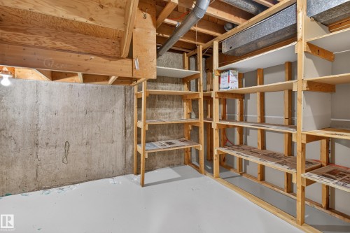 Unfinished basement area featuring exposed wood framing, concrete foundation walls, a light gray painted floor, and extensive built-in wooden shelving for storage - 17603 85 Avenue Nw, Edmonton, AB 