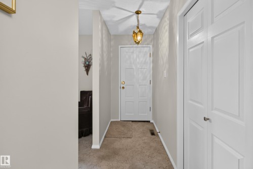 Entryway featuring a paneled door with brass hardware, a brass chandelier, and white baseboards - 17603 85 Avenue Nw, Edmonton, AB 