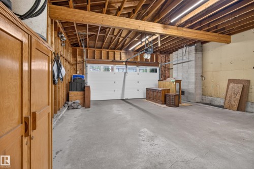 Spacious garage featuring a concrete floor, exposed wood beam ceiling, and a white overhead garage door - 17603 85 Avenue Nw, Edmonton, AB 