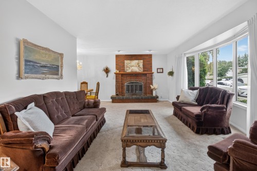 Living area featuring a brick fireplace with a raised hearth, a large bay window, and light-toned carpeting - 17603 85 Avenue Nw, Edmonton, AB 