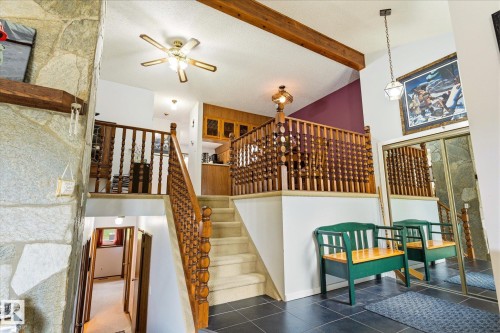 Stone accent wall with a wooden mantel, dark tile flooring, and a multi-level staircase featuring wooden banisters - 59 Patterson Crescent, St. Albert, AB - Indoor Photo Showing Other Room