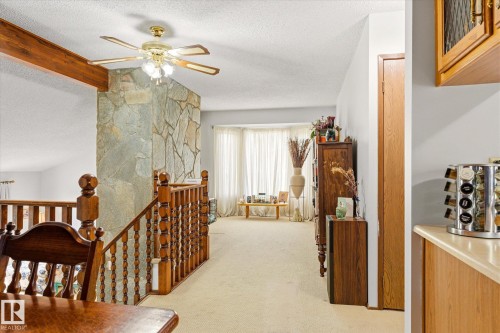 Open-concept living space featuring a stone accent wall, wood staircase with balusters, and a ceiling fan with light fixture - 59 Patterson Crescent, St. Albert, AB - Indoor Photo Showing Other Room