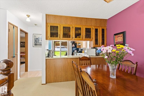 Dining area featuring wood-finish paneling, overhead cabinetry with glass inserts, and a pass-through counter to the kitchen - 59 Patterson Crescent, St. Albert, AB - Indoor Photo Showing Dining Room