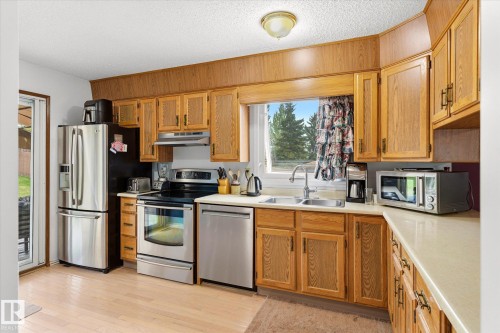 Kitchen featuring light wood-finish cabinetry, stainless steel appliances, a double basin sink, light-toned countertops, and light wood-finish flooring - 59 Patterson Crescent, St. Albert, AB - Indoor Photo Showing Kitchen With Double Sink