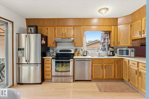 Kitchen featuring wood-finish cabinetry, stainless steel appliances, light countertops, and wood-finish flooring - 59 Patterson Crescent, St. Albert, AB - Indoor Photo Showing Kitchen With Double Sink