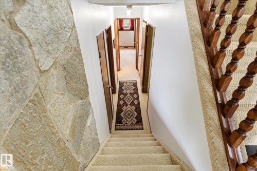 Carpeted staircase with turned wood balusters and a stone accent wall - 59 Patterson Crescent, St. Albert, AB - Indoor Photo Showing Other Room