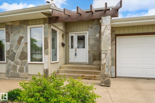 Stone veneer facade featuring an integrated garage, a covered entry, and prominent windows, complemented by mature shrubbery - 59 Patterson Crescent, St. Albert, AB - Outdoor