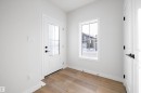 Entryway featuring a white paneled door with glass inserts and black hardware, wood-finish flooring, a white window with grid detailing, and crisp white walls - 954 Elderberry Landing, Edmonton, AB 