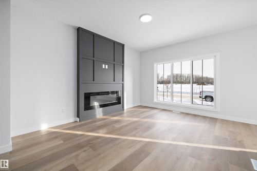 Spacious living area featuring a dark gray accent wall with an integrated linear fireplace, large picture window, light wood-finish flooring, and recessed ceiling lighting - 954 Elderberry Landing, Edmonton, AB 