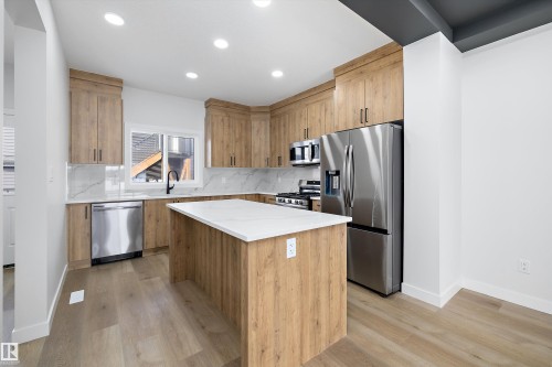 Kitchen featuring a central island with white countertop, wood-finish cabinetry, stainless steel appliances, and wood-finish flooring - 954 Elderberry Landing, Edmonton, AB 