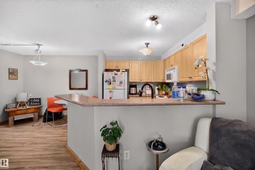 Kitchen featuring a breakfast bar with stone-finish countertop, light wood cabinetry, and stainless steel appliances - 414 11214 80 Street, Edmonton, AB 