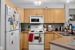Functional kitchen featuring light wood-finish cabinetry and a white appliance suite including a built-in microwave and refrigerator - 
