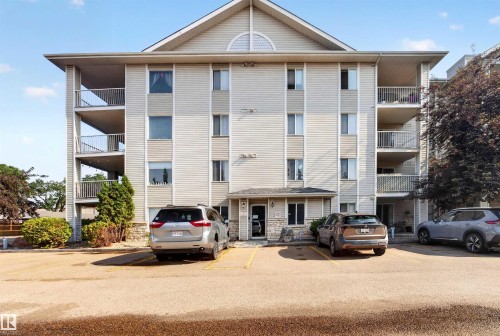 Multi-story building with light-toned siding, multiple balconies with metal railings, and a stone facade entry - 414 11214 80 Street, Edmonton, AB 