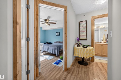 Interior hallway with wood-finish flooring, leading to a bedroom featuring a ceiling fan and a bathroom with a wood vanity - 414 11214 80 Street, Edmonton, AB 