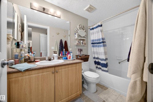 Bathroom featuring a vanity with a light wood-finish cabinet, integrated sink, and a large wall-mounted mirror - 414 11214 80 Street, Edmonton, AB 