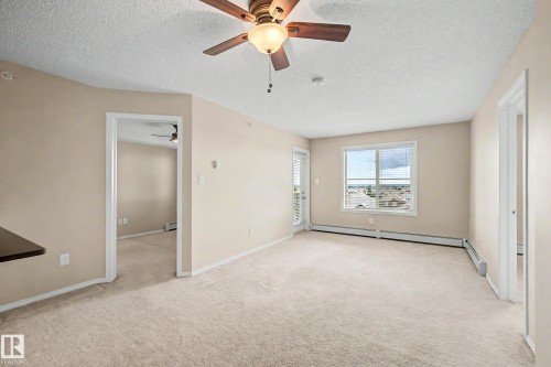 Carpeted living space featuring a ceiling fan with light fixture, a window with blinds, and a door to an exterior balcony - 404 1080 Mcconachie Boulevard, Edmonton, AB 