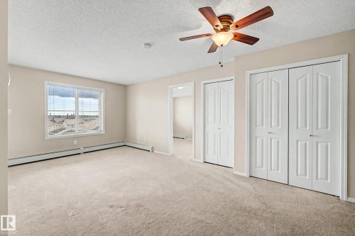 Spacious room featuring neutral carpet flooring, a window offering exterior views, two bi-fold panel doors, and a ceiling fan with integrated lighting - 404 1080 Mcconachie Boulevard, Edmonton, AB 