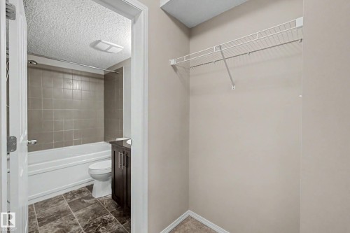 Bathroom featuring a white bathtub with neutral-toned tiled surround, a dark wood-finish vanity, and patterned tile flooring - 404 1080 Mcconachie Boulevard, Edmonton, AB 