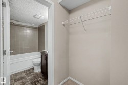 Bathroom featuring a white bathtub with neutral-toned tiled surround, a dark wood-finish vanity, and patterned tile flooring - 