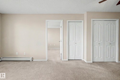 Carpeted interior space featuring neutral wall paint, a white baseboard heater, and multiple white bi-fold doors - 404 1080 Mcconachie Boulevard, Edmonton, AB 