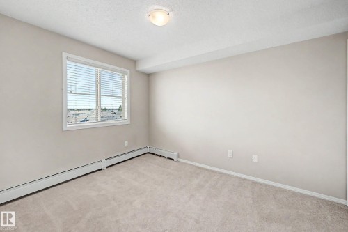 Carpeted room featuring a large window with blinds, neutral wall paint, and baseboard heating - 404 1080 Mcconachie Boulevard, Edmonton, AB 