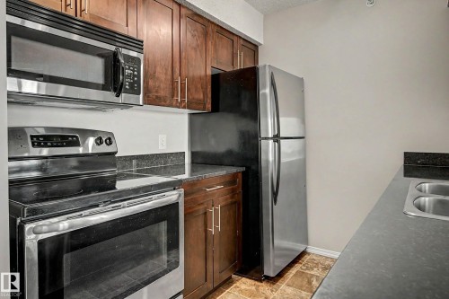 Kitchen featuring stainless steel appliances, dark wood cabinetry, and a double-basin sink - 404 1080 Mcconachie Boulevard, Edmonton, AB 