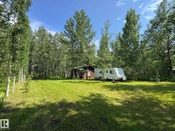 Expansive cleared area surrounded by mature trees, featuring a brown-sided structure and a white recreational vehicle - 