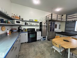 Functional kitchen area featuring a full-size black range, stainless steel refrigerator, and ample counter space with open shelving - 