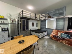 Open-concept living area featuring concrete flooring, a custom built-in loft bed structure, and a window with a roller shade - 