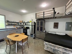 Open-concept living space featuring a full kitchen with light gray cabinetry and open shelving, a built-in elevated sleeping area, and durable concrete flooring - 