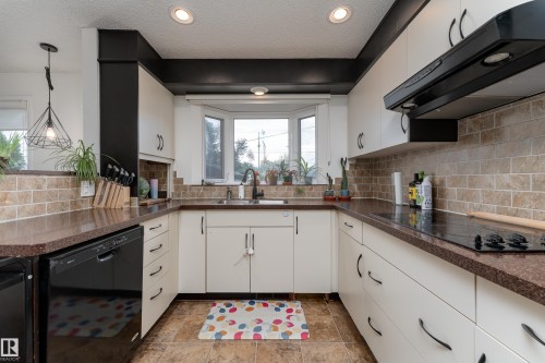 U-shaped kitchen featuring white cabinetry, dark countertops, a tile backsplash, recessed lighting, and a bay window - 13616 137 Street, Edmonton, AB 