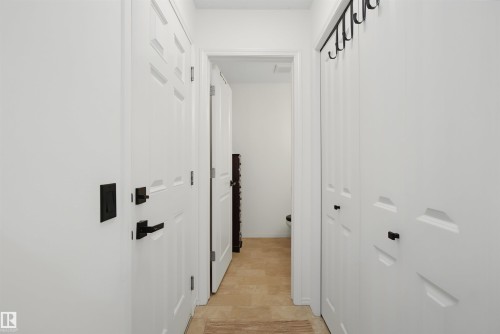 Hallway featuring white paneled doors with matte black hardware - 15 450 Hyndman Crescent, Edmonton, AB 