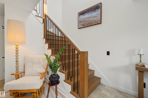 Hardwood staircase with black metal balusters and wood handrails, light-toned walls, and tile flooring - 15 450 Hyndman Crescent, Edmonton, AB 