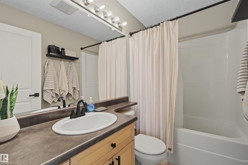 Bathroom featuring a light wood-finish vanity with a dark countertop, an oval undermount sink, and a black faucet - 15 450 Hyndman Crescent, Edmonton, AB 