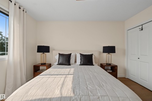 Bedroom featuring a large window with white curtains, light-toned walls, and wood-finish flooring - 15 450 Hyndman Crescent, Edmonton, AB 