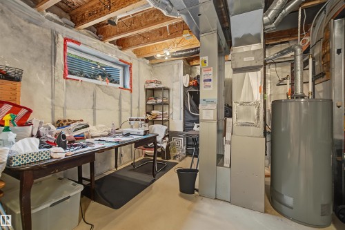 Unfinished basement area featuring exposed ceiling joists, a horizontal window well, concrete walls, and utility hookups - 15 450 Hyndman Crescent, Edmonton, AB 