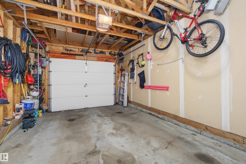 Single-bay garage featuring a concrete floor, exposed wood ceiling joists, and a white panel garage door with an automatic opener - 15 450 Hyndman Crescent, Edmonton, AB 