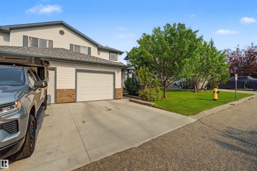 Two-story property featuring light-colored siding, a dark shingle roof, and an attached two-car garage - 15 450 Hyndman Crescent, Edmonton, AB 