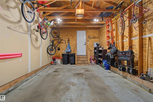 Concrete floor garage featuring an exposed wood beam ceiling, exposed wood stud walls, and a white access door with a small landing - 15 450 Hyndman Crescent, Edmonton, AB 