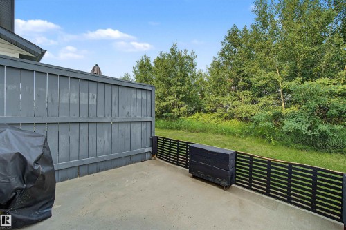 Outdoor patio with concrete flooring, a partial privacy fence, and a horizontal slat perimeter fence, bordered by mature trees - 15 450 Hyndman Crescent, Edmonton, AB 