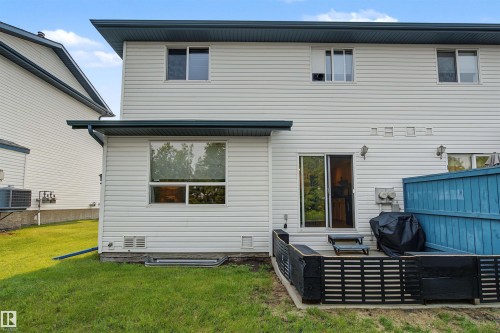 Rear exterior featuring white vinyl siding, a ground-level patio with dark fencing, and a sliding glass door - 15 450 Hyndman Crescent, Edmonton, AB 
