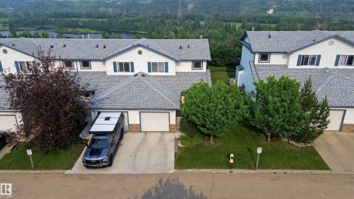Townhome exterior featuring white siding, grey shingle roofing, and blue louvered shutters - 15 450 Hyndman Crescent, Edmonton, AB 