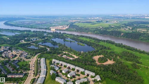 Aerial perspective showcasing multiple residential developments surrounded by extensive green spaces, a winding river, and several natural ponds - 15 450 Hyndman Crescent, Edmonton, AB 