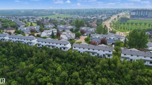 Townhome community featuring multiple two-story residences with light-colored siding and gray shingle roofs - 15 450 Hyndman Crescent, Edmonton, AB 