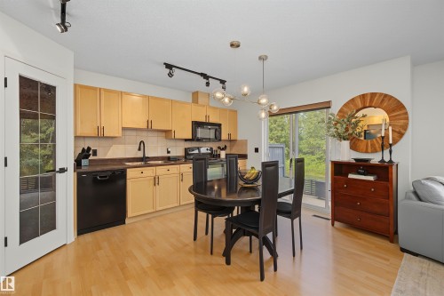 Open-concept kitchen featuring light wood cabinetry, black appliances, and a tile backsplash - 15 450 Hyndman Crescent, Edmonton, AB 
