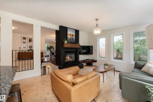 Living area featuring a black brick fireplace with a wood mantle, multiple windows, and light-toned flooring - 7816 142 Street, Edmonton, AB 