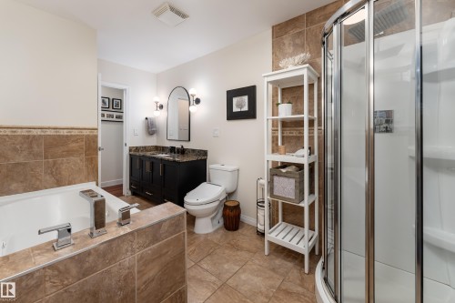 Bathroom featuring a vanity with a patterned countertop, undersink basin, matte black faucet, a built-in soaking tub with deck-mounted fixtures, a curved glass shower enclosure, and floor-to-ceiling tile. - 7816 142 Street, Edmonton, AB 